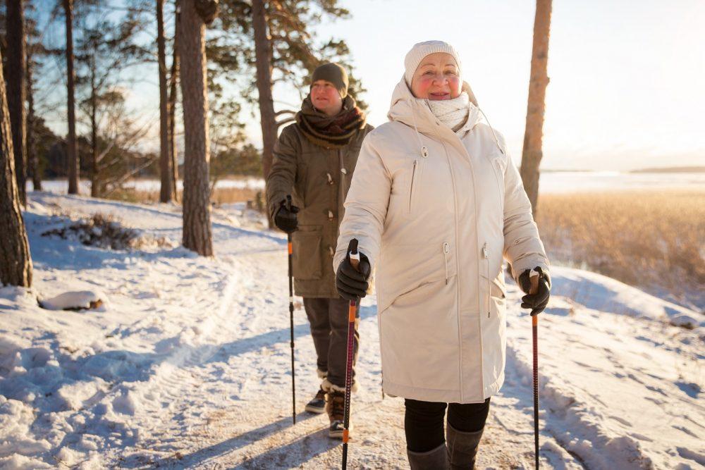 Kuvituskuva. Kaksi henkilöä sauvakävelylenkillä. Kuvan henkilöt kävelevät pitkin lumista metsäpolkua keskellä talvea.